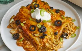 two chicken enchiladas (Angela's Awesome Enchiladas) garnished with black olives, sliced scallions, and a dollop of sour cream on a white plate