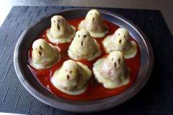 a plate of 7 cheese-draped mini meatloaves shaped like ghosts in a pool of tomato sauce