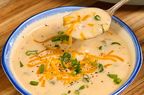 A bowl of cheesy potato soup garnished with green onions and shredded cheese