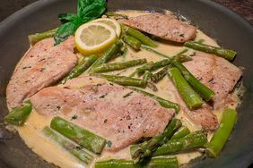 skillet with chicken cutlets, asparagus spears, and lemon cream sauce