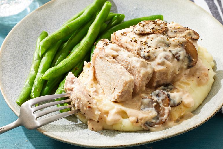 Plate with a serving of pork chop in cream of mushroom sauce mashed potatoes and green beans fork visible on the side