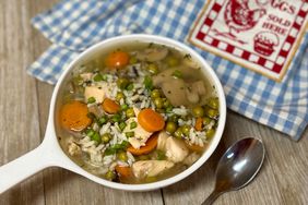bowl of chicken rice vegetable soup on plank table with blue check napkin and spoon