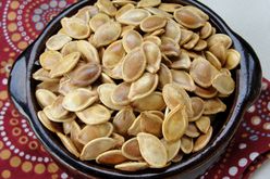top-down view of golden brown pumpkin seeds in a ceramic bowl