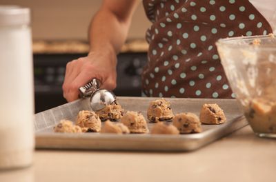 Person placing cookie dough scoops on a baking sheet using a scoop
